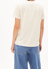 Cremefarbene T-Shirts mit kurzen Ärmeln aus Baumwolle, kombiniert mit lockeren blauen Jeans. Einfaches, lässiges Design ohne sichtbare Markenlogos.