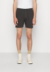 Shorts de sport noirs avec une taille élastique et un cordon de serrage, associés à des chaussettes beiges et des baskets montantes crème.