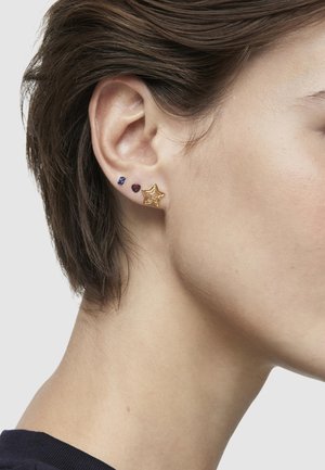 Orecchino a stella dorata con tre orecchini aggiuntivi: pietra azzurra, cuore borgogna e piccola pietra blu scuro, posizionati su una pelle chiara.