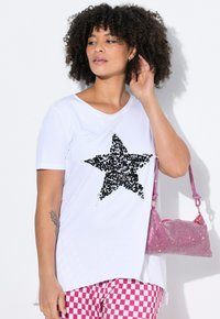 Hvid T-shirt med en stor sort pailletstjerne, parret med lyserøde ternede bukser og en lyserød paillet-handbag. Korte ærmer, afslappet pasform.