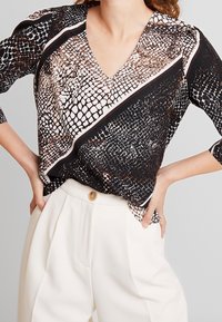 Blusa nera e beige con un motivo a pelle di serpente, caratterizzata da una scollatura a V, maniche a tre quarti e un design asimmetrico con strisce a contrasto.