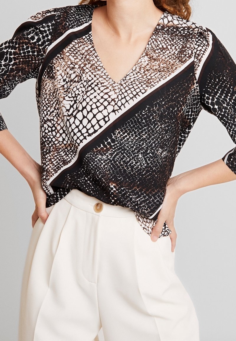 Blusa nera e beige con un motivo a pelle di serpente, caratterizzata da una scollatura a V, maniche a tre quarti e un design asimmetrico con strisce a contrasto.