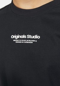 Czarny bawełniany t-shirt z okrągłym dekoltem. Zawiera biały nadruk: "Originals Studio", "Dostarczone przez JACK&JONES" oraz "Zaprojketowane w Kopenhadze."