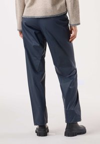 Navy waterproof pants with a smooth texture, elastic waistband, and snap closures at the cuffs, paired with chunky black boots.