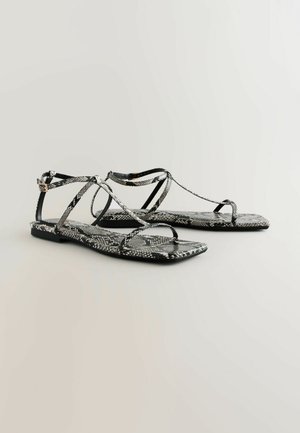 Sandali piatti con motivo a serpente bianco e nero, caratterizzati da cinghie incrociate e una piccola fibbia decorativa. Texture liscia e forma rettangolare.