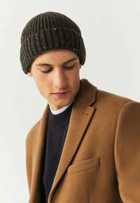 Knit beanie in dark gray with ribbed texture and speckles, paired with a brown wool-blend coat featuring a notch lapel and chest pocket.