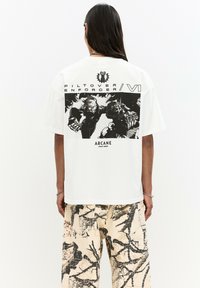Valkoinen unisex T-paita, jossa on musta graafinen printti selässä, tekstillä "Pilt-over Enforcer VII" ja "ARCANE", lyhyet hihat ja rento fit.