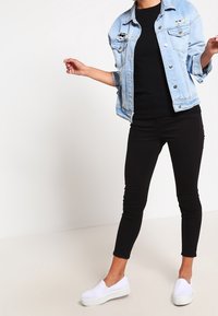 Ljusblå denimjacka med slitna detaljer, svart åtsittande topp, svarta skinny jeans och vita slip-on sneakers.