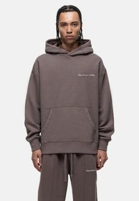 Felpa grigiaoversize realizzata in morbido tessuto, con una tasca frontale e cappuccio regolabile con coulisse. Ricamo discreto sul petto.