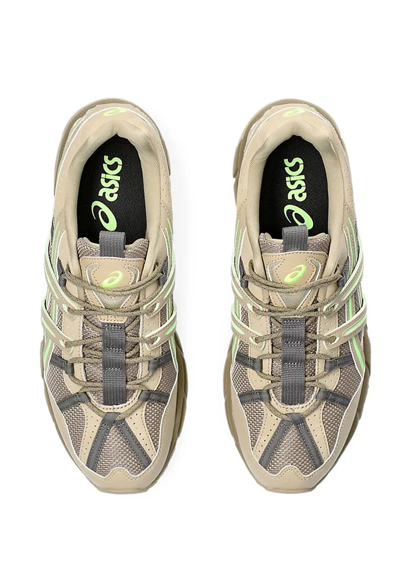 Zapatillas deportivas beige con parte superior de malla y sintético. Presentan detalles reflejantes en verde, cordones grises y una plantilla negra acolchada.