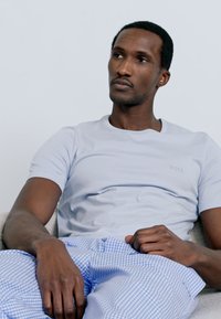 Svetlo modra majica z okrolim izrezom in subtilnim logotipom, kombinirana z modrimi in belimi kariranimi pižamastimi hlačami. Gladek material in sproščen kroj.