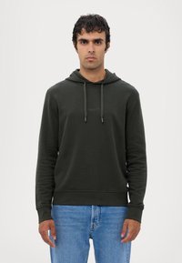 Grønn hettegenser med snøring, ribbestrikkede mansjetter og kant. Myk stoff, minimal merkevare på brystet, kombinert med blå jeans.