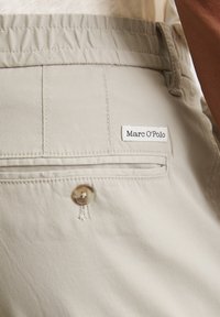 Beige broek van zacht materiaal met een gestructureerd oppervlak, voorzien van een zijzak, een knoopsluiting en een klein Marc O'Polo logo label.