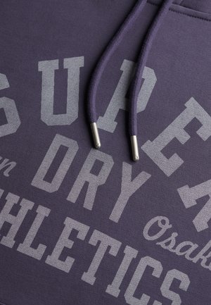 Paarse sweatshirt met grote grijze tekst "SUPER DRY ATHLETICS" en "Osaka." Voorzien van bijpassende trekkoorden met zilverkleurige metalen uiteinden.