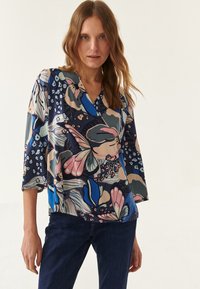 Blusa multicolorida con un patrón floral y abstracto, escote en forma de V y amplias mangas de tres cuartos, hecha de una tela suave.