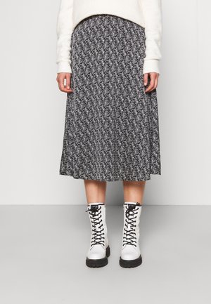 Person iført en sort og hvid blomsterprint midi-nederdel, hvid blød sweater og hvide snørestøvler på en grå gulv.