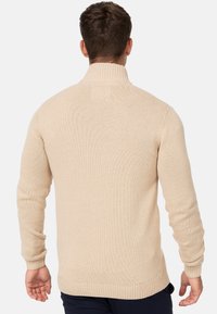 Beige gebreide trui met een hoge kraag, ribbelmanchetten en zoom. Kenmerkt zich door een gestructureerd patroon en een getailleerd ontwerp.