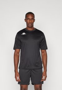 Sort atletisk skjorte og shorts lavet af glat stof. Har korte ærmer og rund hals, med et hvidt Kappa-logo på venstre bryst.