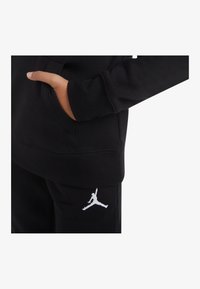 Felpa nera con cappuccio e tasca frontale, maniche lunghe e polsini a coste. Presenta il logo Jumpman bianco sui pantaloni della tuta nera. Tessuto morbido.