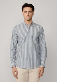 Camisa abotonada con rayas verticales azules y blancas, de mangas largas, con cuello y un bolsillo en el pecho, hecha de una tela ligera.
