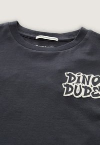 Camiseta de algodón orgánico azul marino con cuello redondo y tejido texturizado, que presenta un prominente gráfico blanco "DINO DUDES" en el pecho.