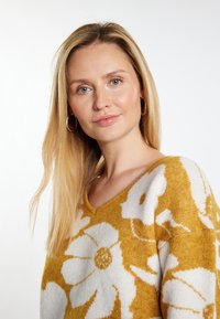 Sweter dzianinowy z dekoltem w serek, z żółtym tłem i dużymi białymi wzorami kwiatowymi. Miękka tekstura i luźny krój.