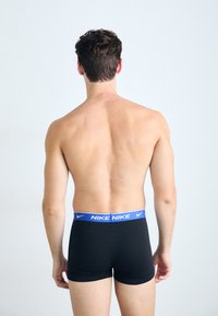 Schwarze Boxershorts mit einem blauen Gummibund, der das "NIKE"-Logo trägt, aus glattem Stoff und in eng anliegender Passform, von hinten gezeigt.