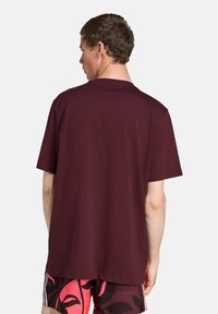 Bordeaux katoenen t-shirt met korte mouwen en een ronde hals, met een eenvoudige achterkant. Gdragen met een kort broek met patroon.
