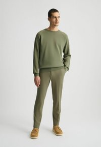 Sudadera verde con mangas raglán combinada con pantalones ajustados a juego. El material parece suave; los zapatos son de ante marrón con suelas blancas.