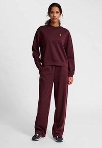 Bordowy zestaw do noszenia w domu składa się z bluzy z okrągłym dekoltem i dopasowanych spodni, wykonanych z miękkiego materiału o luźnym kroju i bocznych kieszeniach.