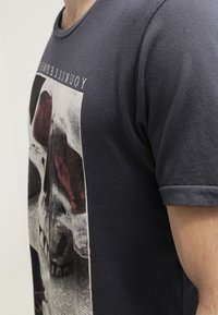 Tmavě šedé bavlněné tričko s velkým grafickým motivem lebky v černé a maroon barvě s textem "Yokilller" nahoře. Krátké rukávy a kulatý výstřih.