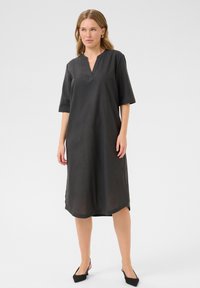 Robe en lin noire avec un décolleté en V, des manches courtes et des fentes latérales. Conception simple, longueur genou, coupe structurée et texture légère.