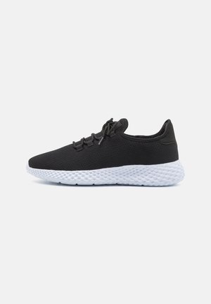 Zapatilla deportiva de malla negra con una suela de goma blanca texturizada y cordones. Diseño ligero con puntera redondeada y cuello acolchado.