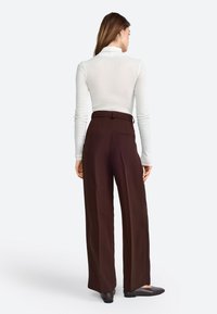 Braune weit geschnittene Hose mit hoher Taille, mit glatter Textur und Gesäßtaschen. Kombiniert mit einem weißen Langarmoberteil.