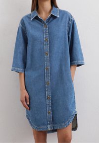 Denimmekko, jossa on napitettava etuosa, lyhyet hihat, terävä kaulus ja pyöreä helma sivuhaalareilla, keskisininen väri.