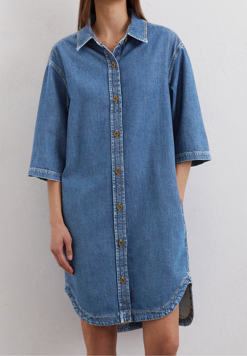 Denimmekko, jossa on napitettava etuosa, lyhyet hihat, terävä kaulus ja pyöreä helma sivuhaalareilla, keskisininen väri.