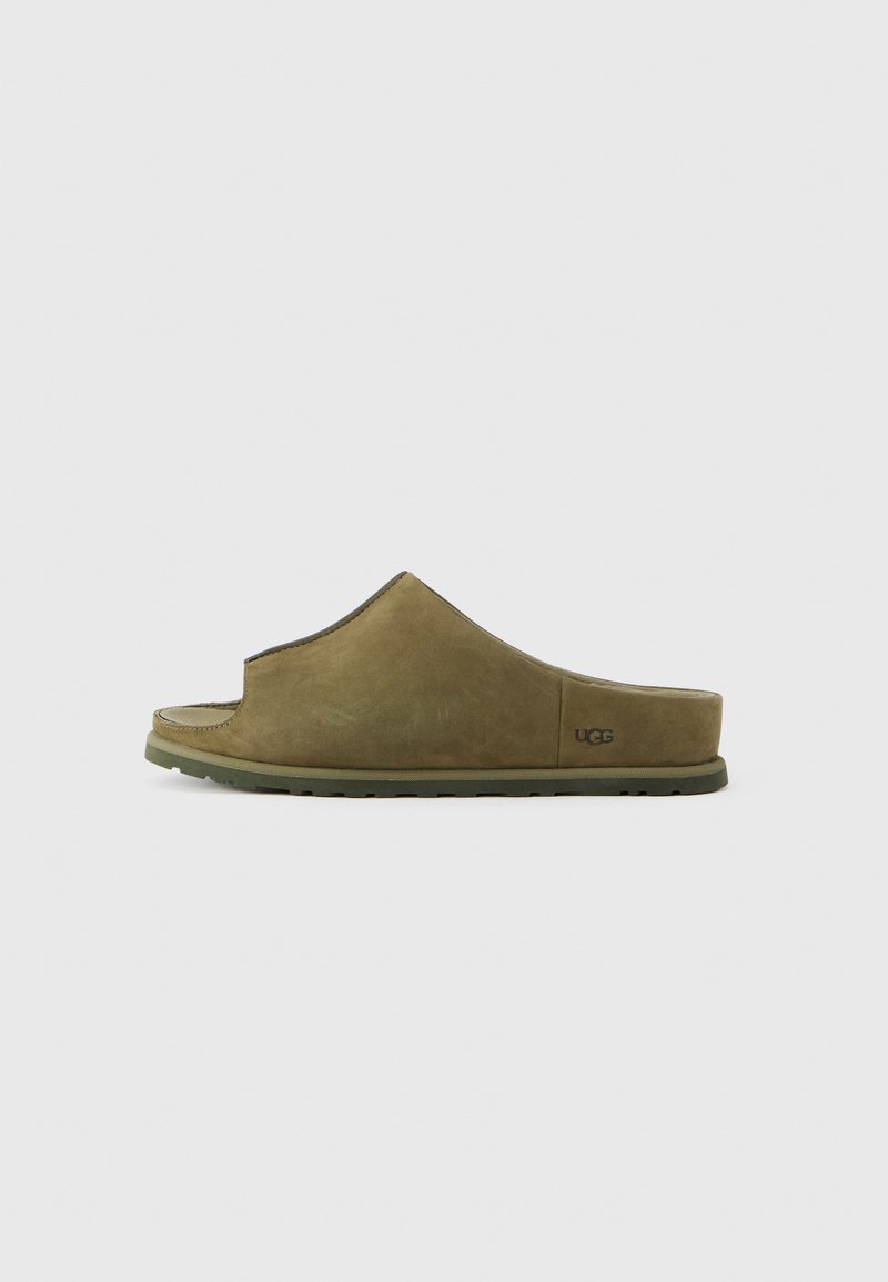 Sandale mule vert olive en daim doux, avec un design à bout ouvert, une large bride et une semelle en caoutchouc texturée. Logo UGG sur le côté.