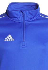 Blaues Zip-Up-Jackett aus strukturiertem Stoff mit hohem Kragen und weißem Adidas-Logo auf der linken Seite. Mit weißen Nähten akzentuiert.