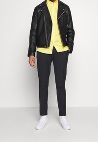 Zwarte leren motorjack, geel overhemd met knopen, donkergrijze slim-fit broek en witte sneakers. Eenvoudig ontwerp, gladde textuur.
