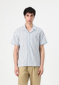 Camisa de botones de manga corta en azul claro con rayas verticales oscuras, hecha de tela suave. Tiene un cuello tipo camp y cierre de botones en la parte frontal.