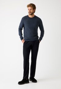 Maglione blu navy con motivo a rombi, collo rotondo e polsini a costine, abbinato a pantaloni neri e scarpe nere. La texture appare liscia.