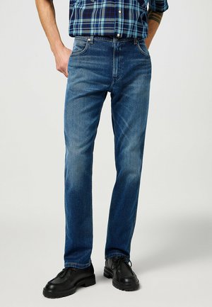 Blauwe denim jeans met een recht gesneden ontwerp, voorzien van een vervaagde textuur en klassieke zakken, gedragen met zwarte schoenen.