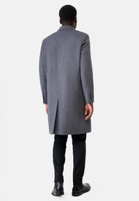 Grijze wollen overjas met een gestructureerd ontwerp, lange rugventilatie en omgeslagen kraag. Gecombineerd met zwarte broek en strakke zwarte laarzen.