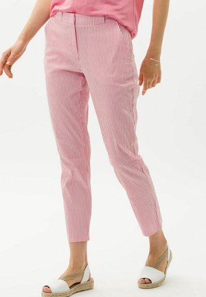 Nainen, joka pukeutuu vaaleanpunaisiin ja valkoisiin pystysuoriin raitahousuihin, vaaleanpunaiseen toppiin ja valkoisiin espadrille-sandaaleihin, joissa on beige nauhat.