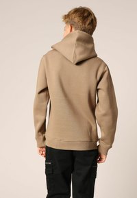 Beige capuchontrui met een gladde textuur, geribbelde manchetten en zoom, gedragen met zwarte cargobroek met ritszakken.