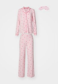 Rosa pyjamas-set med en långärmad knäppblus i röd hjärtformad mönster och kontrasterande kantning, matchad med vida byxor och ögonmask.