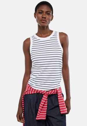 Femme portant un haut blanc sans manches à rayures horizontales noires et un pull rayé rouge et blanc noué autour de sa taille.