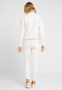 Completo sportivo color beige chiaro con giacca con zip e pantaloni aderenti. Tessuto morbido e liscio con polsini e orlo a coste. Sneakers bianche con accenti rosa.