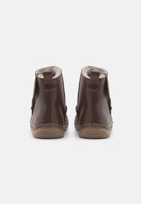 Bottes chelsea en cuir marron avec doublure en fourrure douce, présentant une forme arrondie, des accents cousus et de petites languettes à l'arrière pour un enfilage facile.