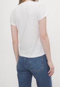 Vit bomull t-shirt med korta ärmar, rund halsringning och en avslappnad passform, tillsammans med blå denimjeans som har bakfickor och sömmar.